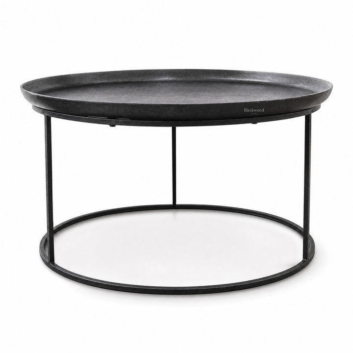 Round antique black coffee table with raised tray-style aluminium top and slender iron frame base for plantation-inspired interiors.