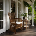 Sika Design DaVinci rattan armchair with high back and white cushion on a porch beside a matching side table and tropical plants.