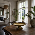 Malabar Centrepiece in vintage brass finish with broad pedestal base on wooden dining table.