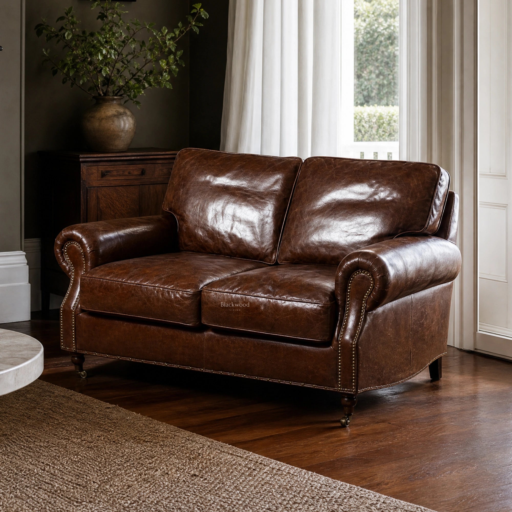 Churchill Two Seat Sofa featuring premium South American top-grain leather upholstery, rolled arms, brass nailhead trim, antique finish, and classic design in a warm living room setting.