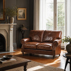 Brown two-cushion leather sofa placed in a living room next to a fireplace