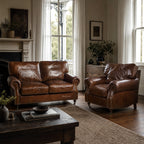 Dark brown leather two-seater sofa in a cozy living room setting, featuring rolled arms, nailhead trim, and antique-finish upholstery.